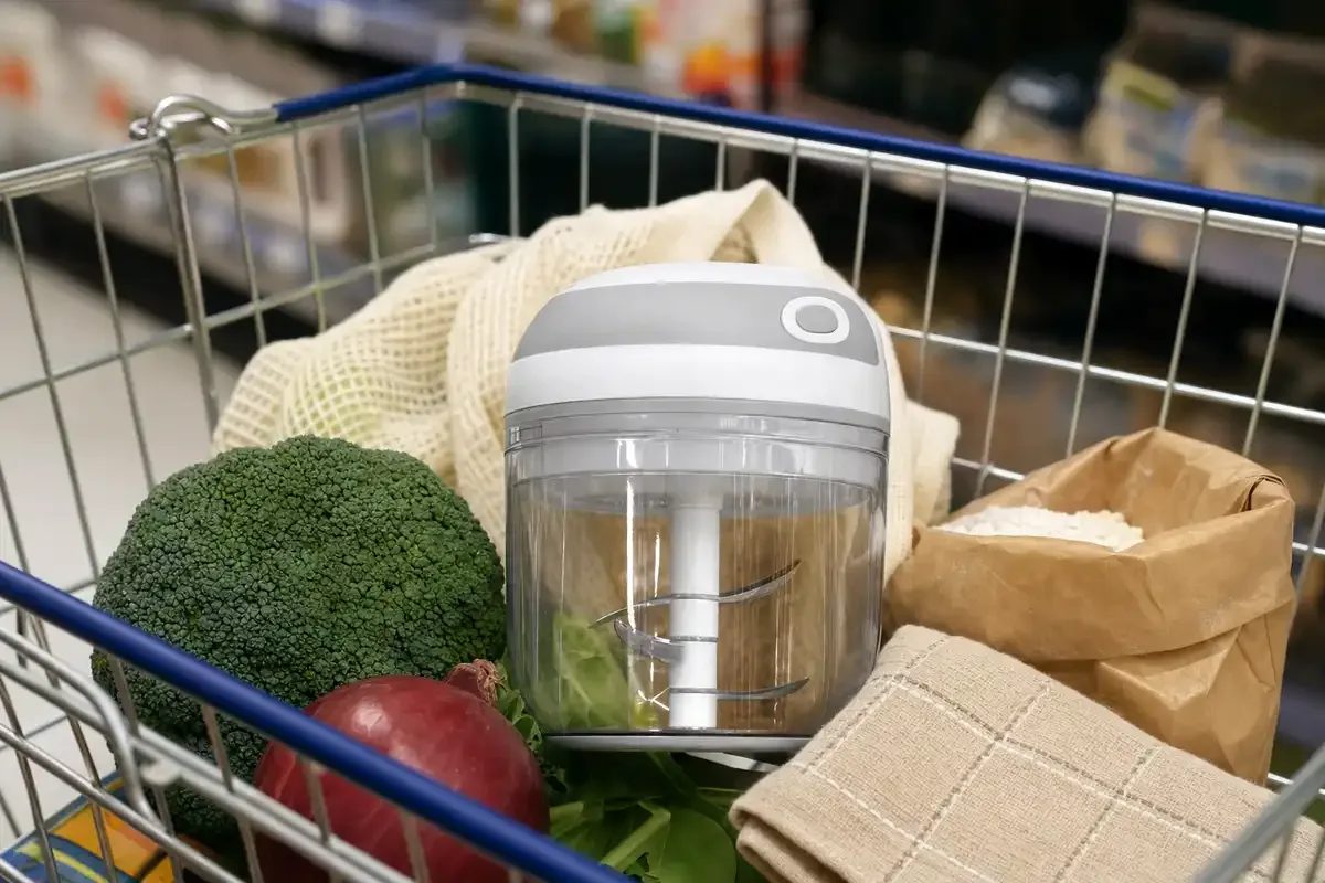 Mini tritatutto cordless in un cestino della spesa, con broccoli, cipolla rossa, sacchetto di farina e strofinaccio