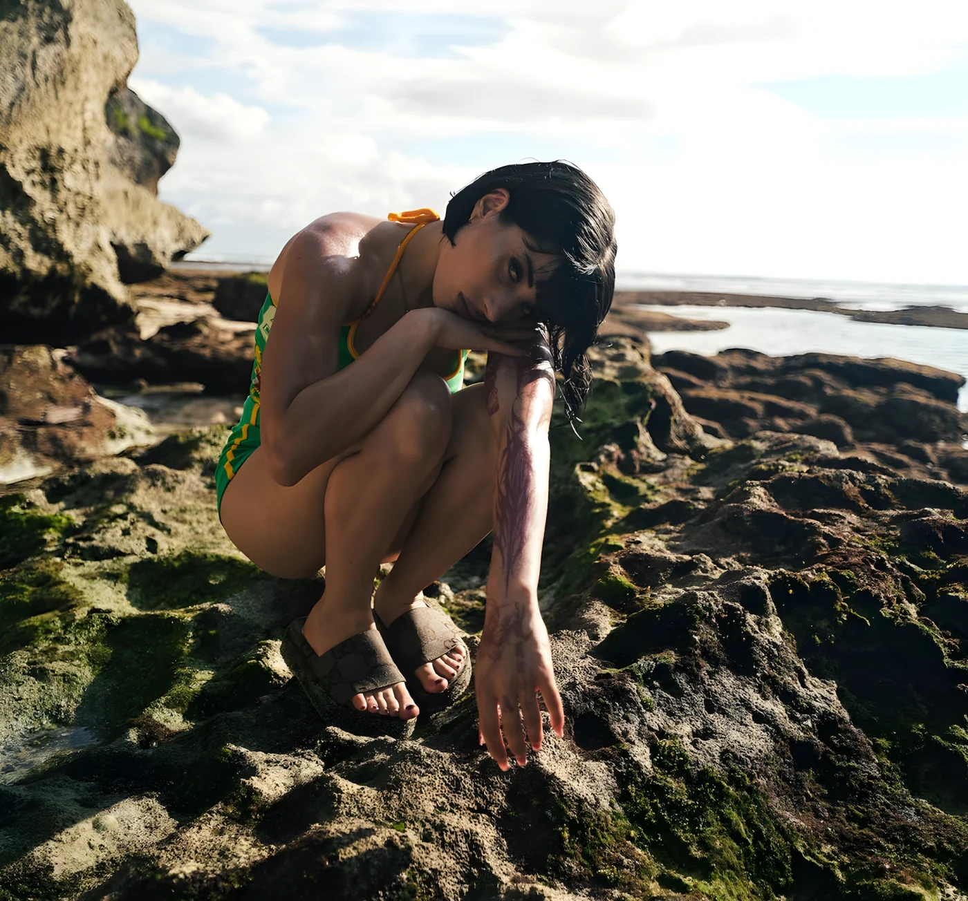 person in a green swimsuit crouching on rocky beach with dramatic lighting.