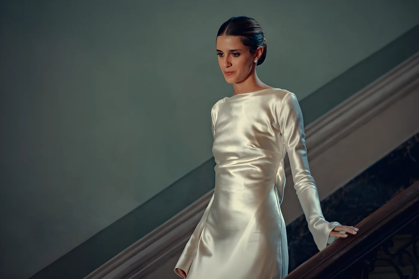 person in a satin dress descending stairs in an elegant setting.