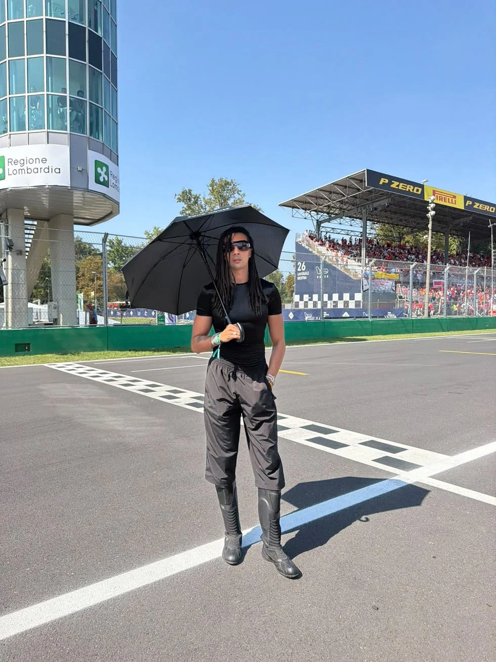 person in black outfit holding umbrella on race track with grandstand background