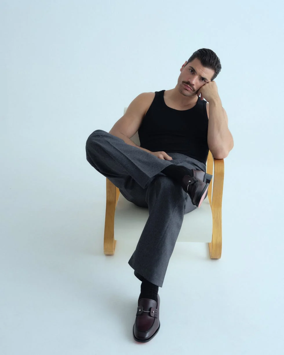 person sitting on a wooden chair wearing a black tank top and gray pants.