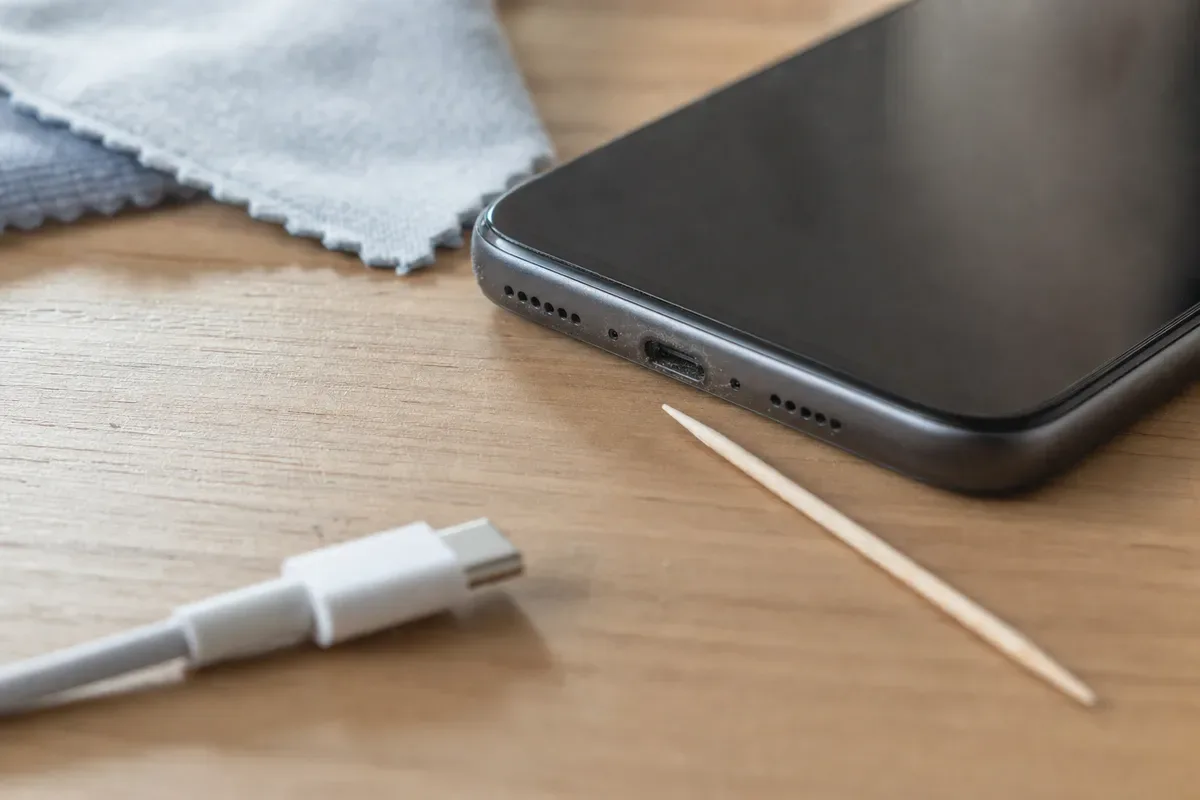 Porta di ricarica di uno smartphone con polvere, stuzzicadenti e cavo USB-C su una scrivania