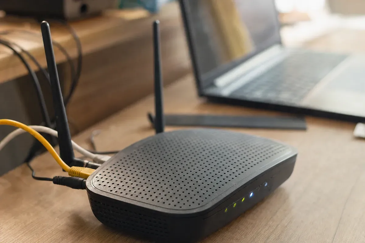 Router Wi‑Fi su scrivania con cavi Ethernet e LED accesi, laptop sfocato sullo sfondo