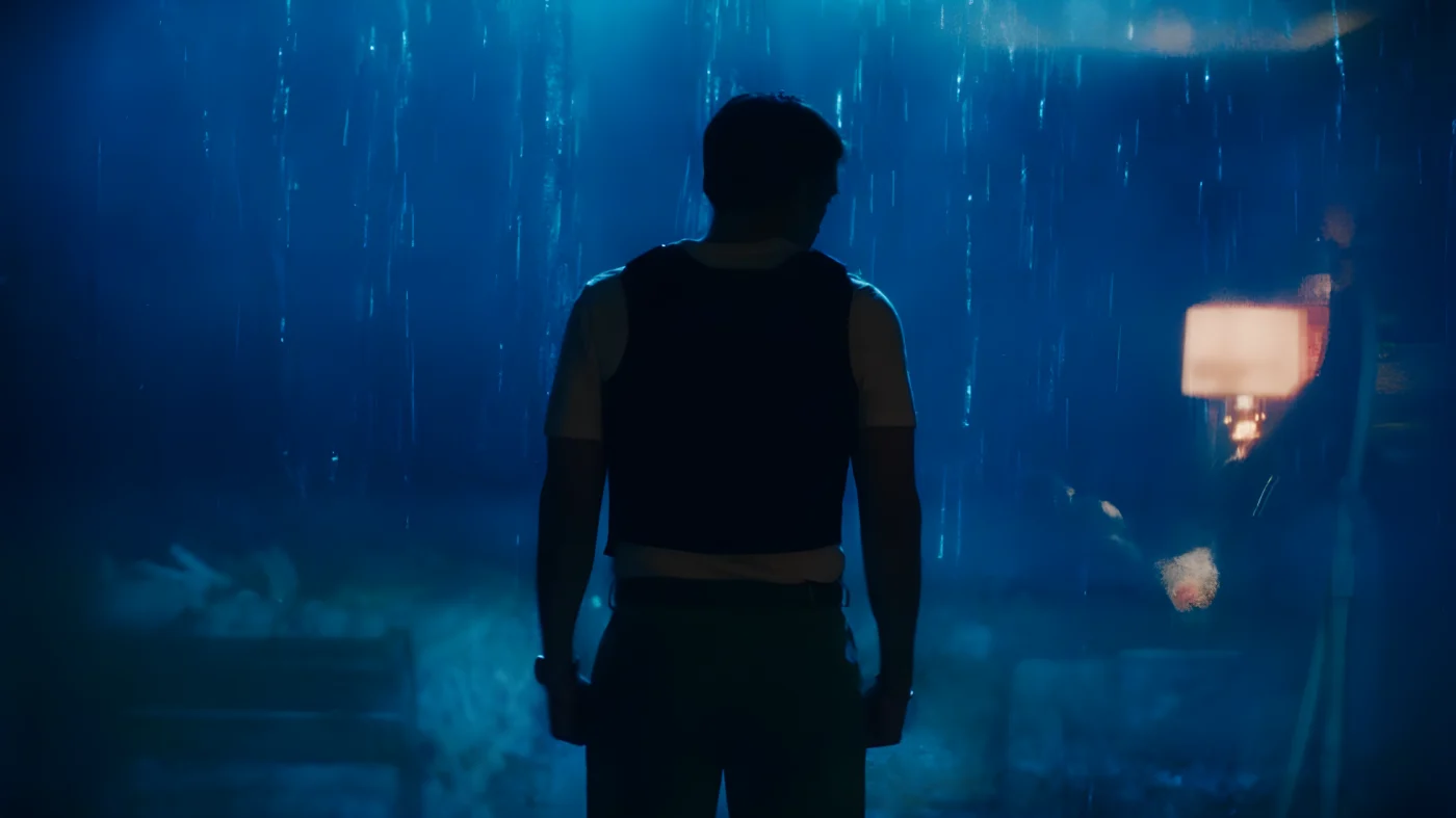 silhouetted person standing in rain with dimly lit background.