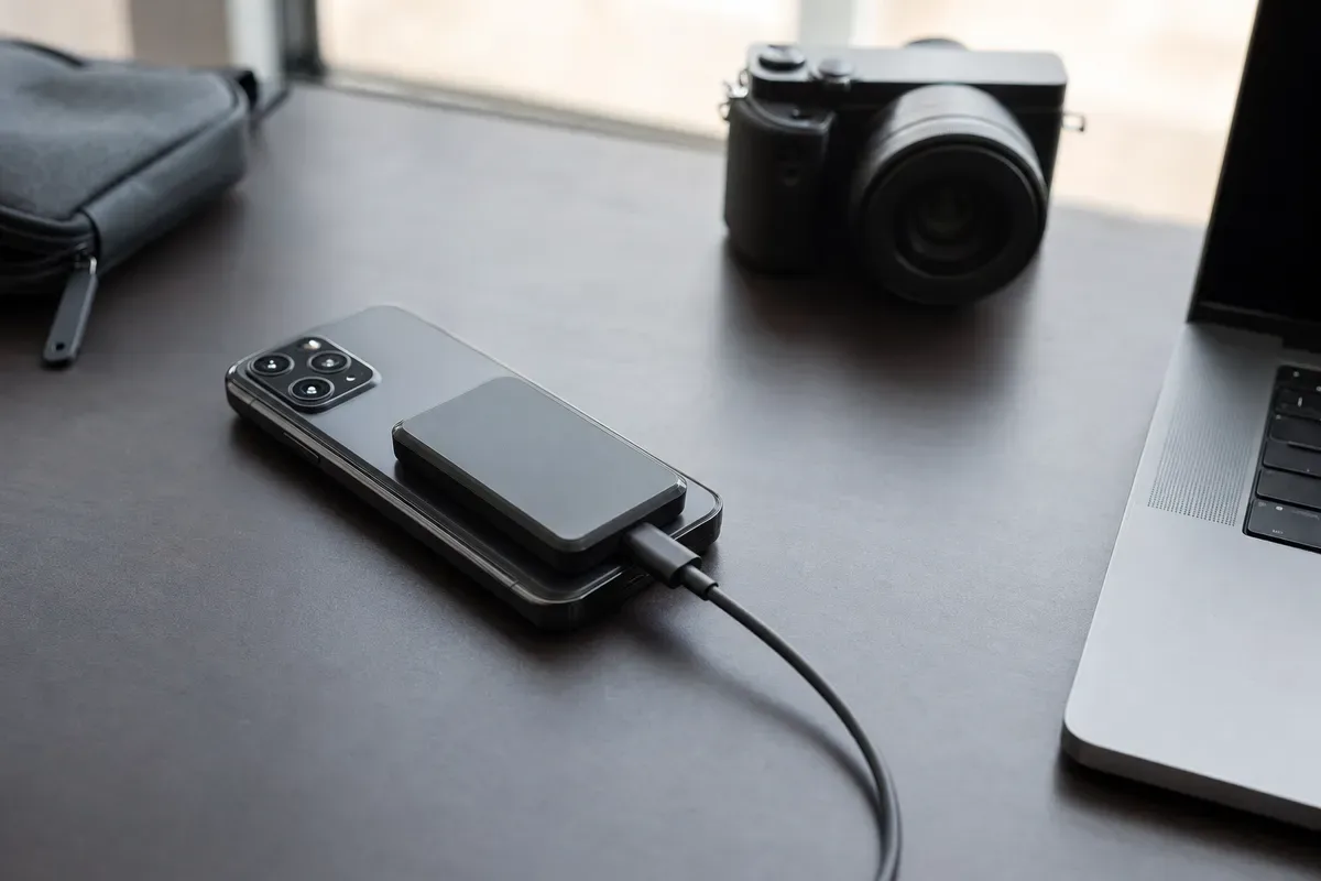 Smartphone con SSD esterno magnetico collegato via USB-C su scrivania, con fotocamera e laptop sullo sfondo