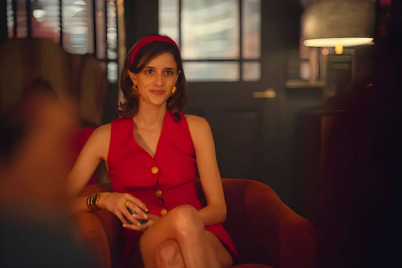 woman in a red dress sitting on a chair, smiling.