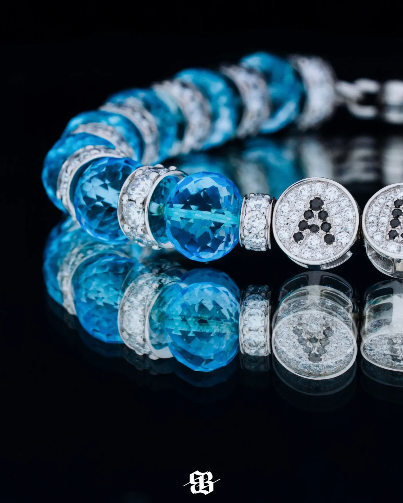 A close-up of a diamond and blue gemstone bracelet with the letter