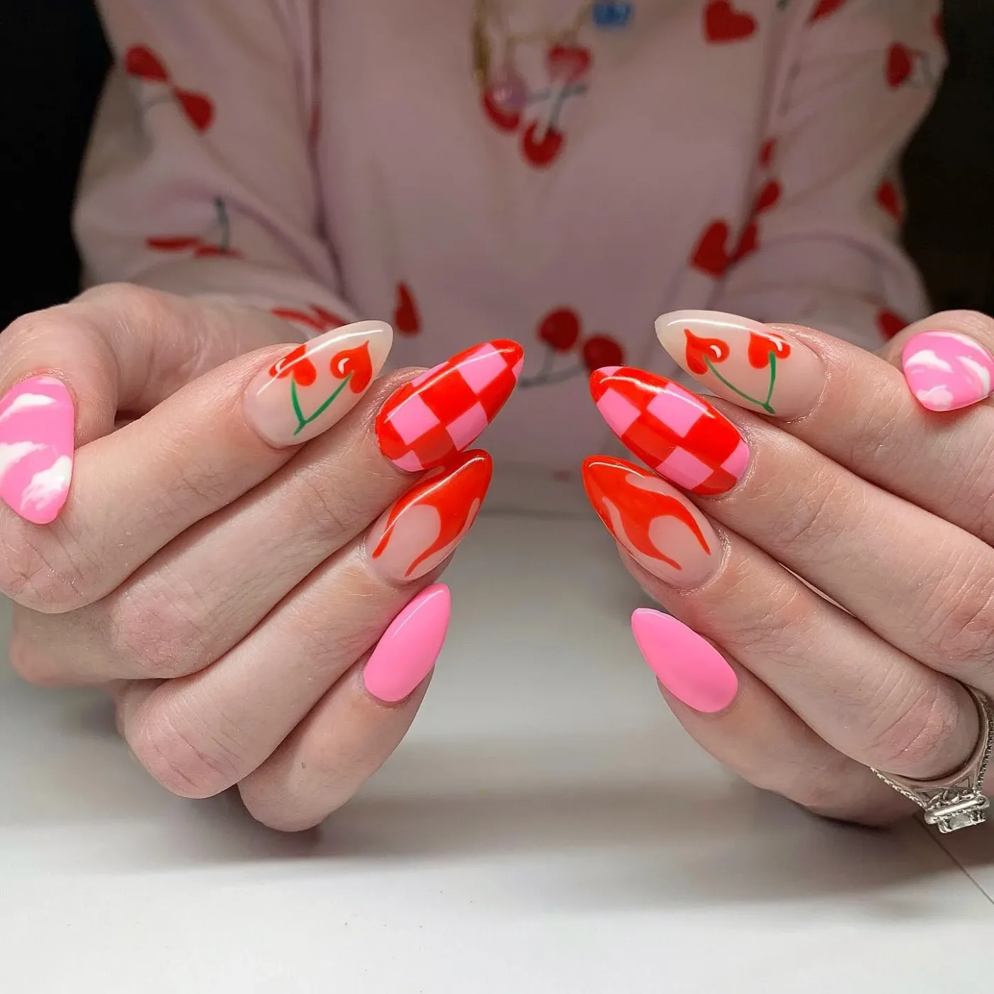 A closeup of hands displaying nail art featuring cherries pink hues and checkered patterns