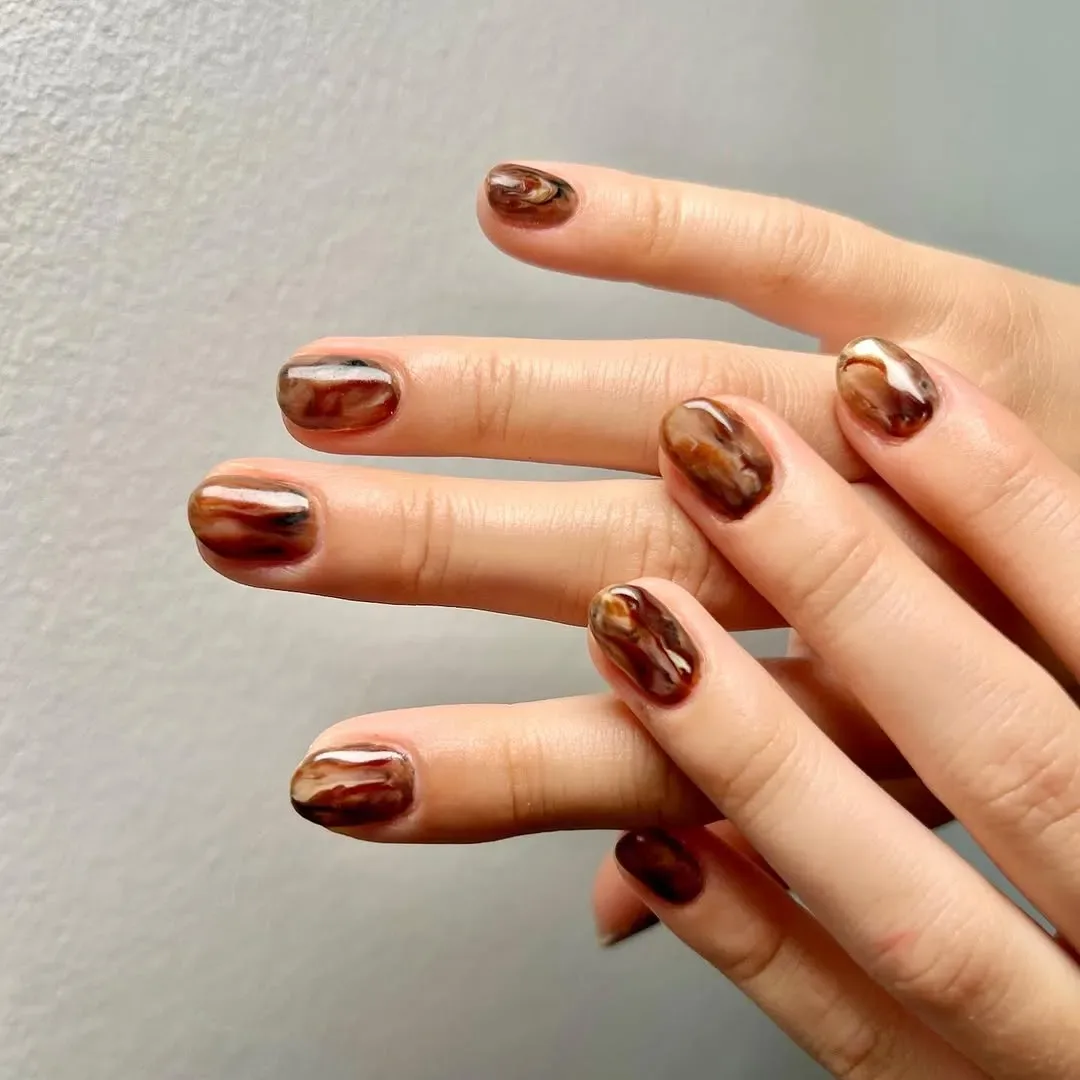 A closeup of hands with metallicstyle nail art on short rounded nails