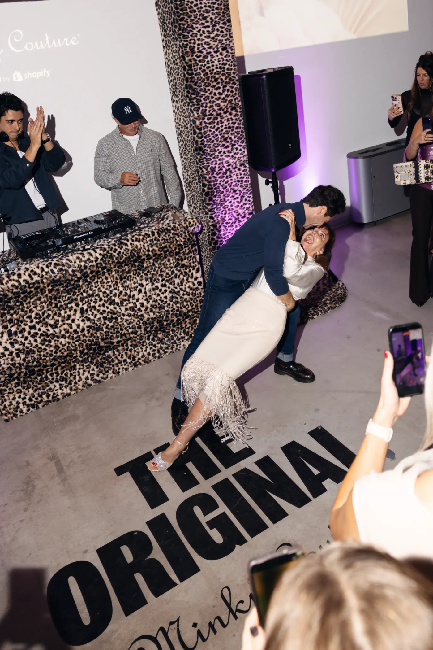 A couple dips and dances inside the Minky Couture pop-up event, with onlookers filming on their phones.