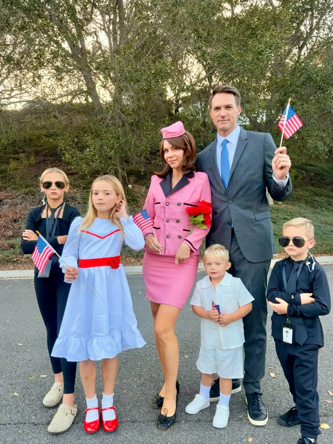 A family of six poses dressed as John F. Kennedy, Jacqueline Kennedy, and their children, holding American flags.
