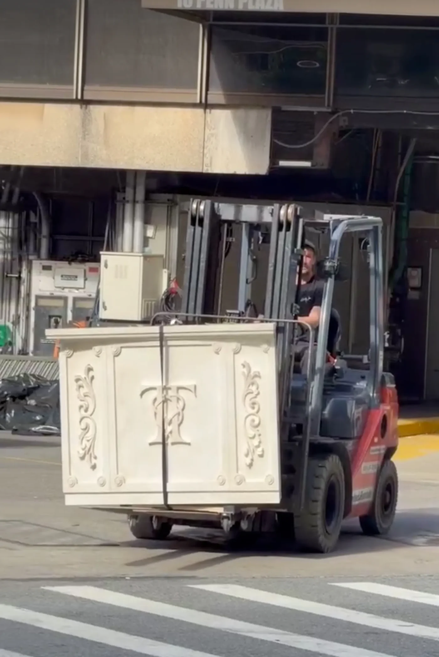 A forklift carrying large white wedding decor with the initials T and T outside Madison Square Garden.