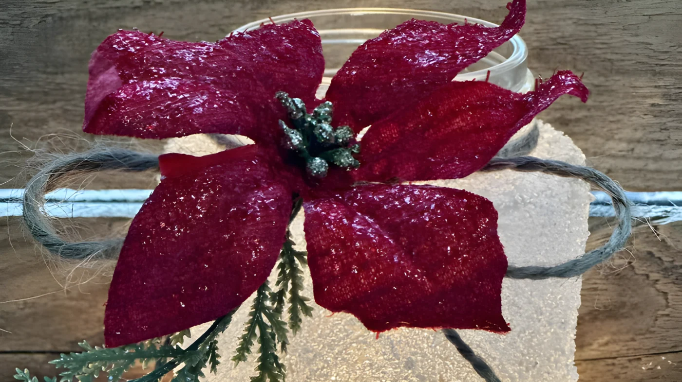 A frosted glass jar decorated with a faux poinsettia and twine.
