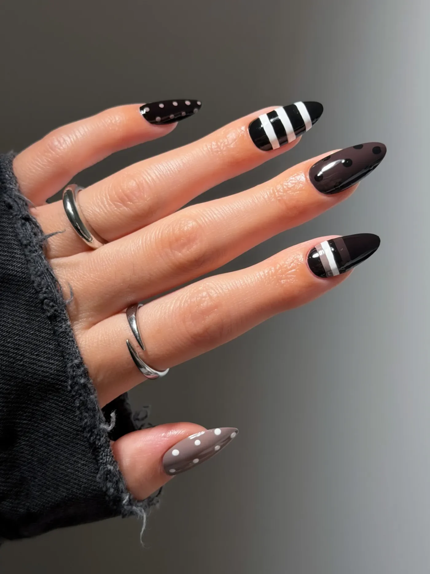 A hand adorned with silver rings nails are styled with black and white designs
