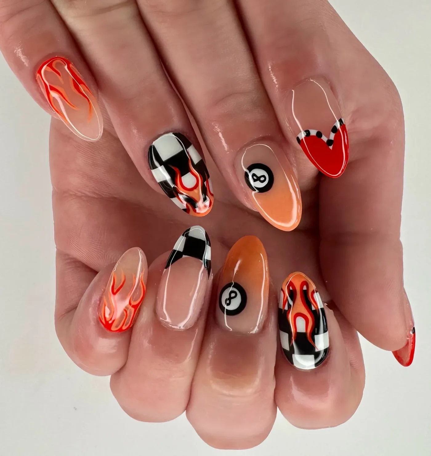 A hand displaying nail art with flame checkered and 8ball designs on different nails