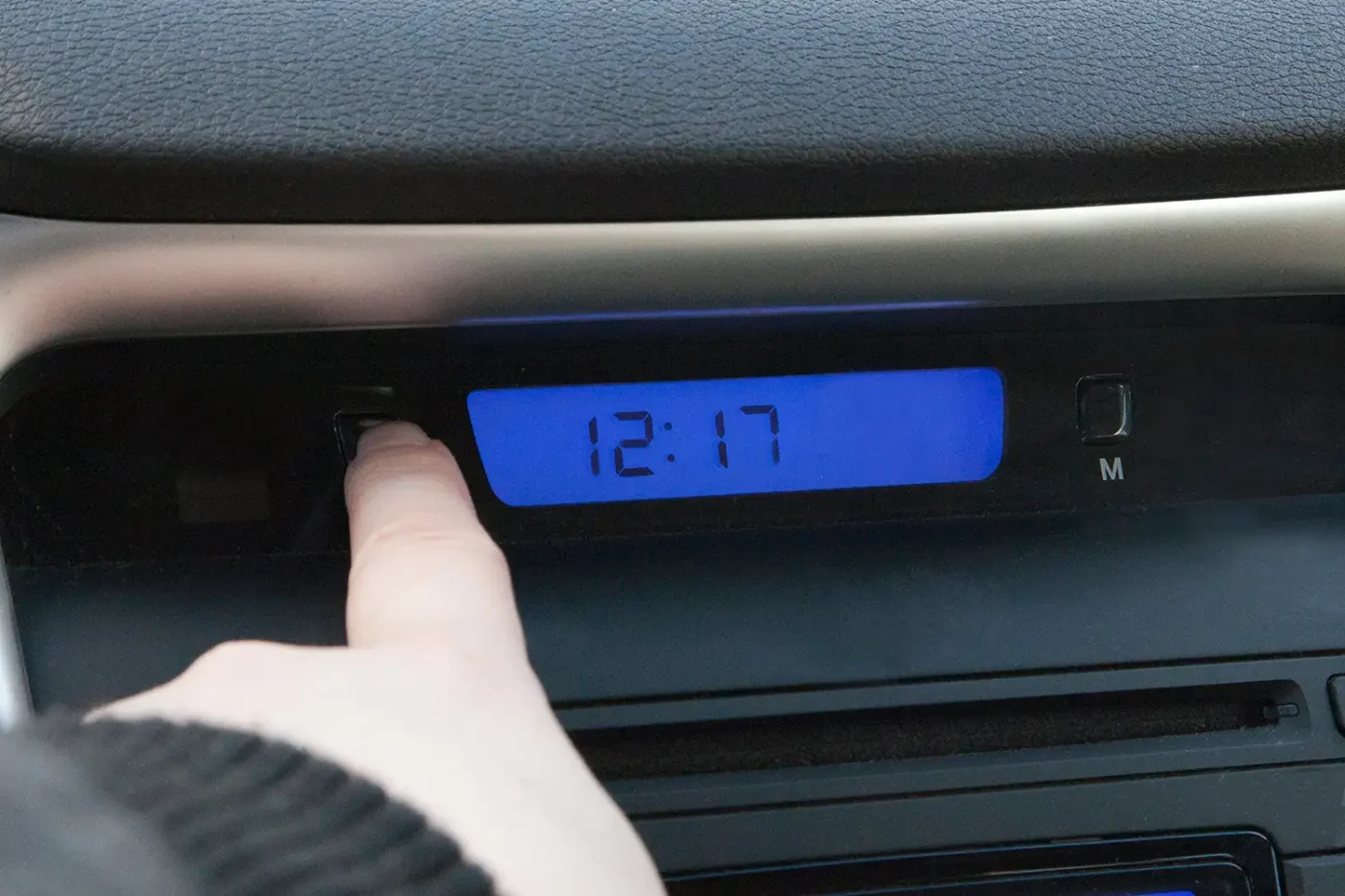 a hand pushes the hour button on a car clock to change the time