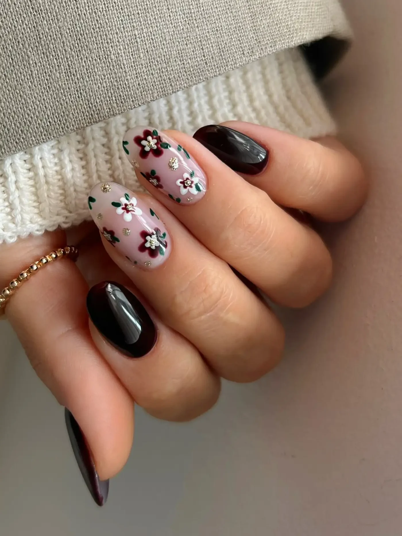 A hand with a manicure featuring black polish and accent nails with floral designs