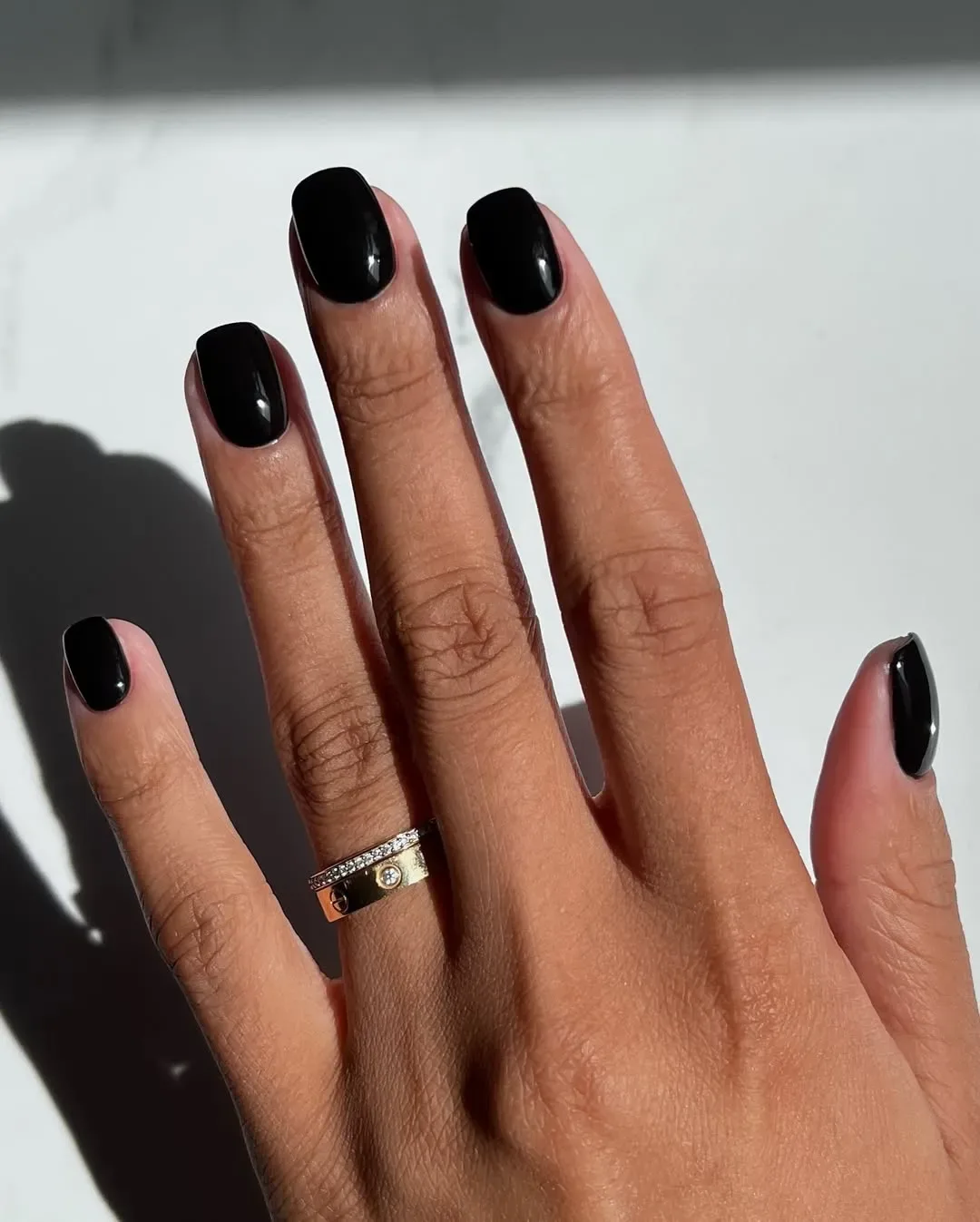 A hand with black nail polish and a gold ring on the ring finger