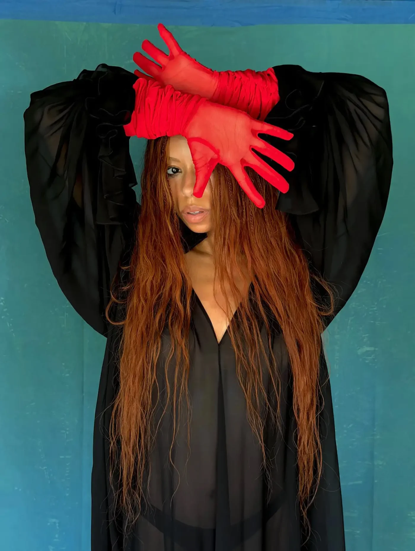 A person posing with red gloves held near their head against a blue background