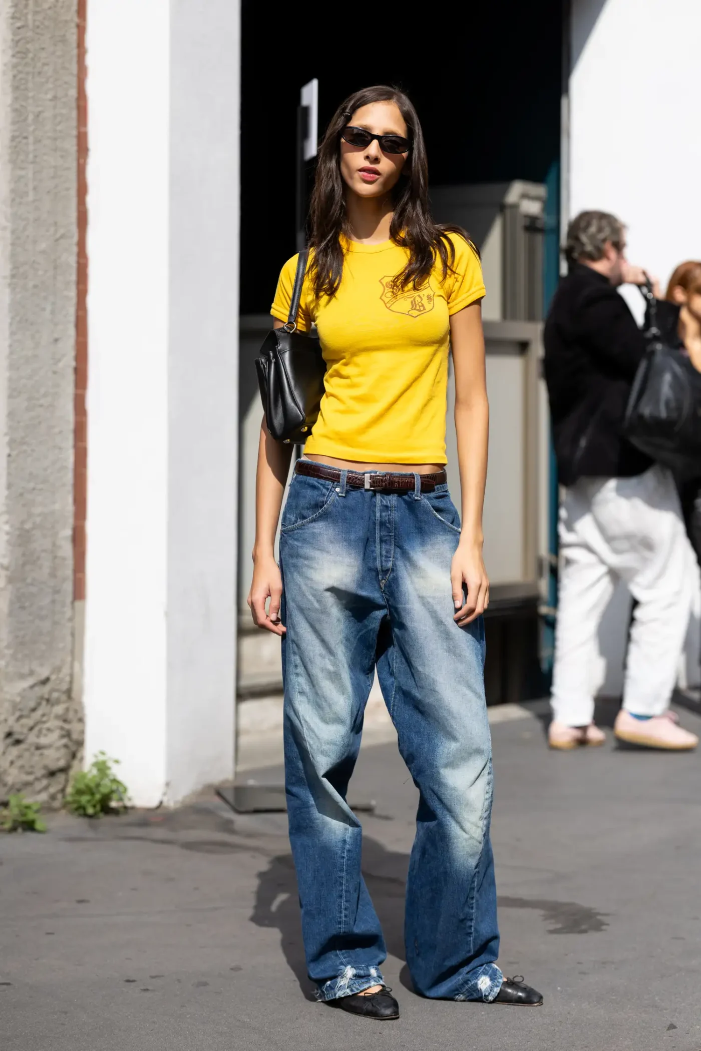 A person standing wearing casual clothing in an urban setting holding a handbag