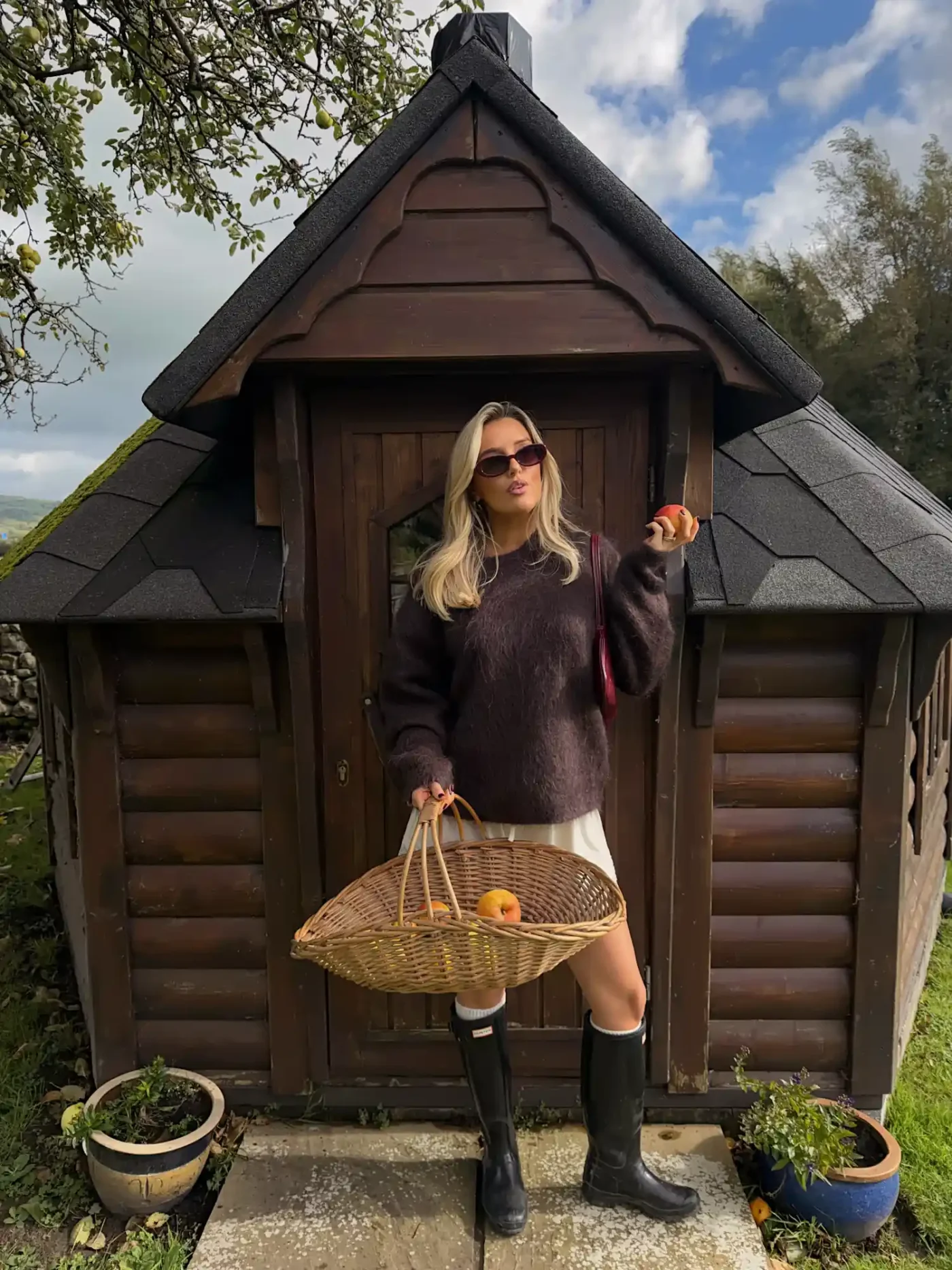 A person stands holding a basket in front of a small wooden structure