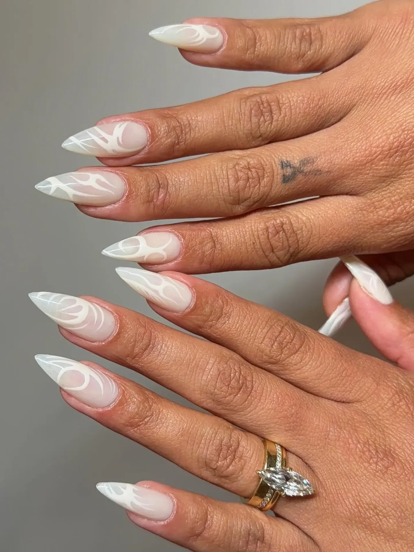 A persons hands showing nails with intricate white art and a visible ring