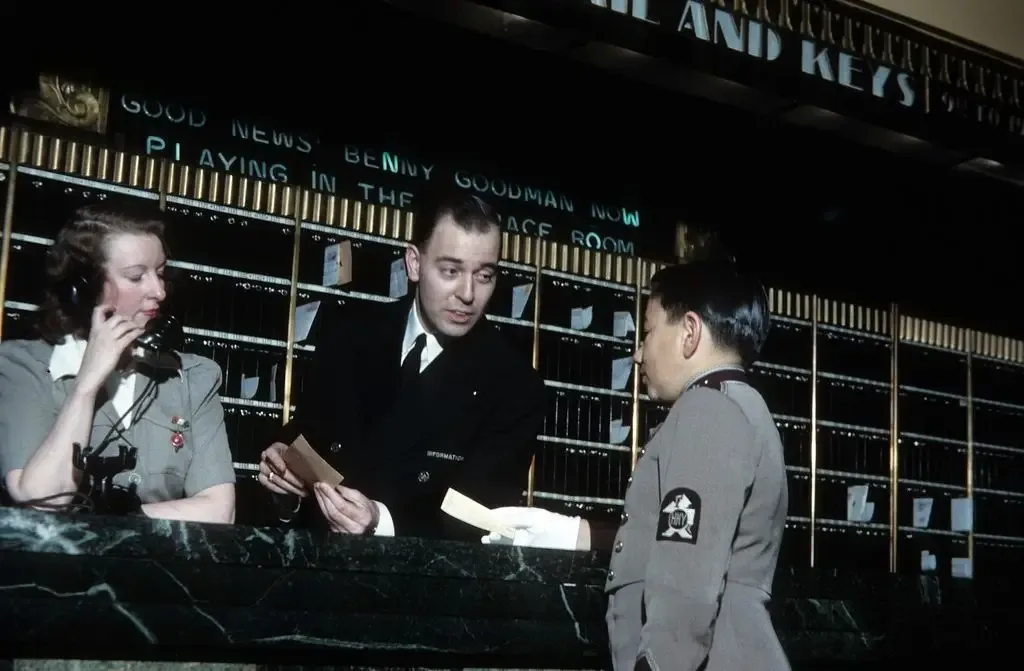 A supervisor at the front desk gives instructions to the porter in The Plaza Hotel in New York, New York, circa 1941