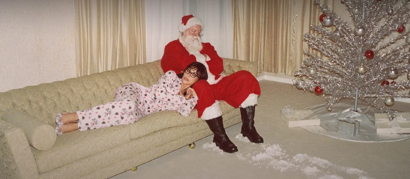 A woman wearing Skims pajamas rests her head on Santa Claus