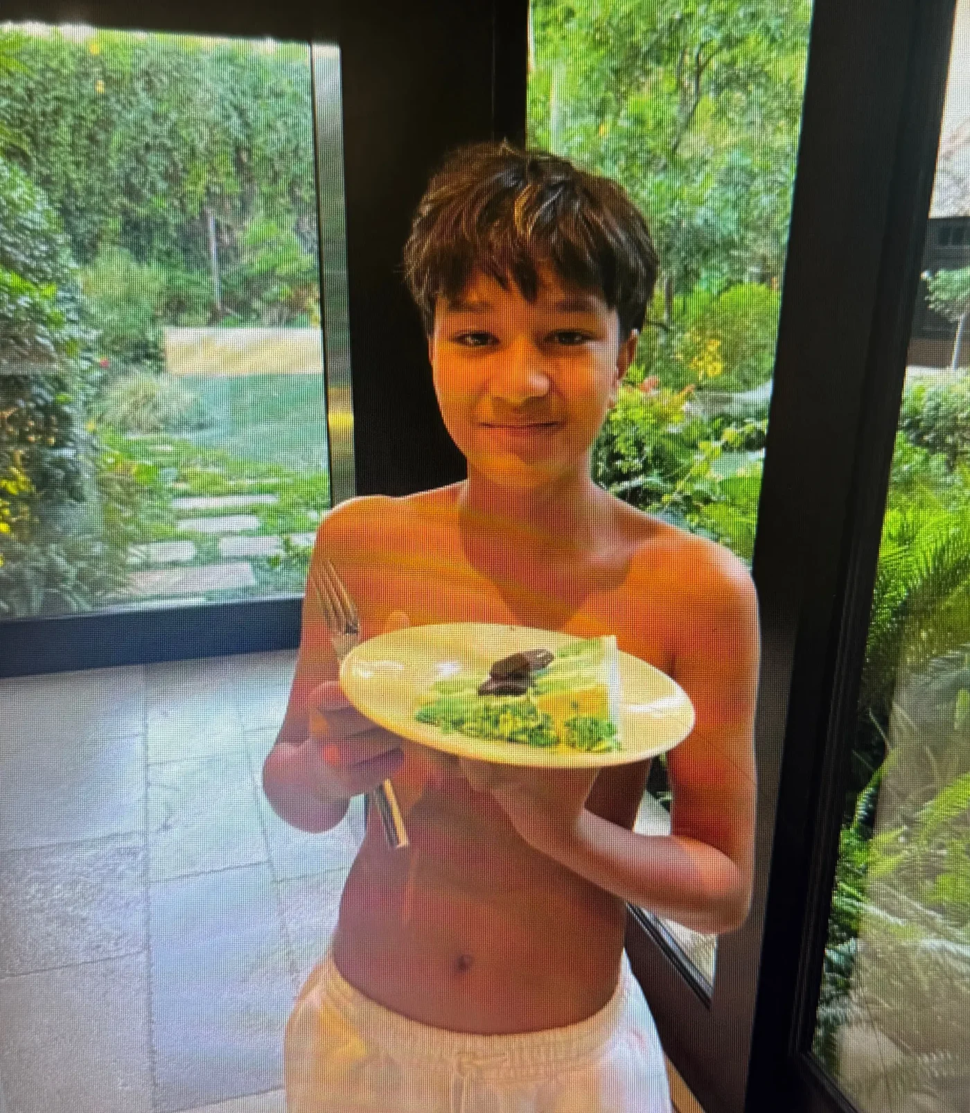 A young boy smiling while holding a plate of food.