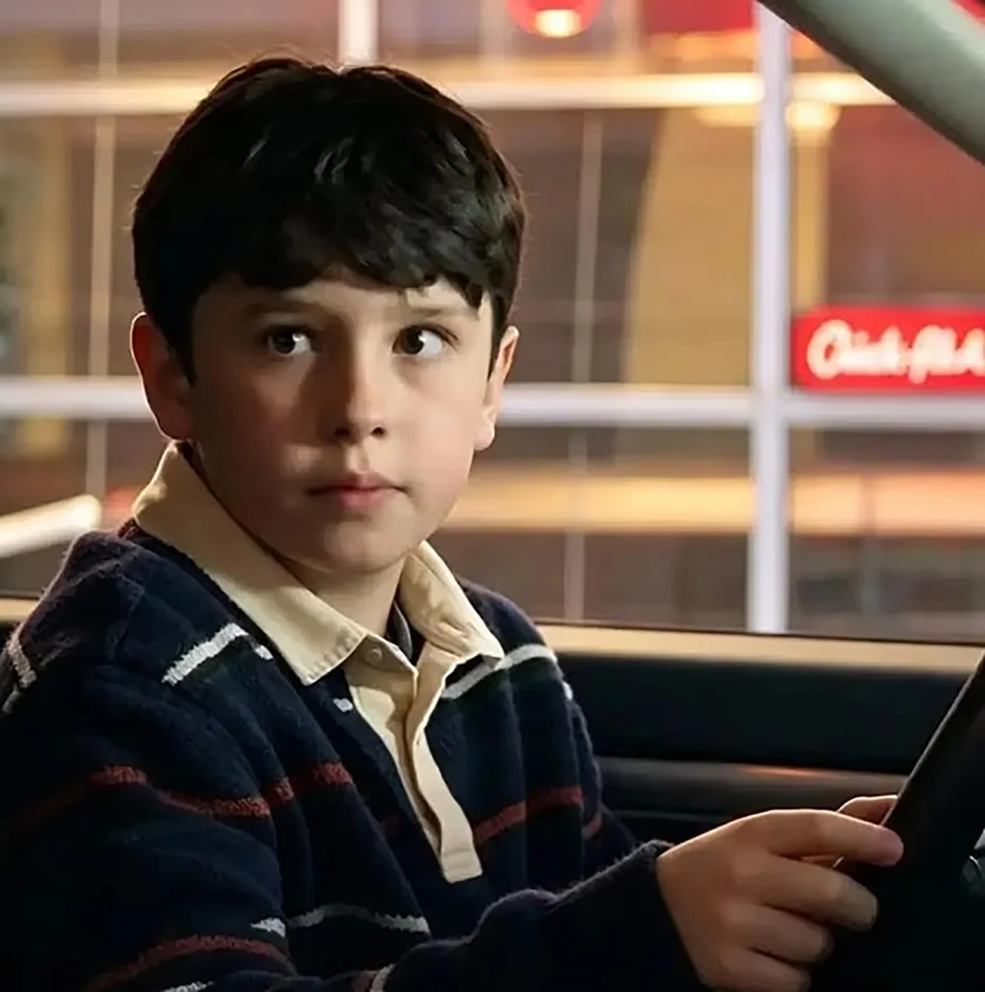 A young boy with dark hair sitting in the driver