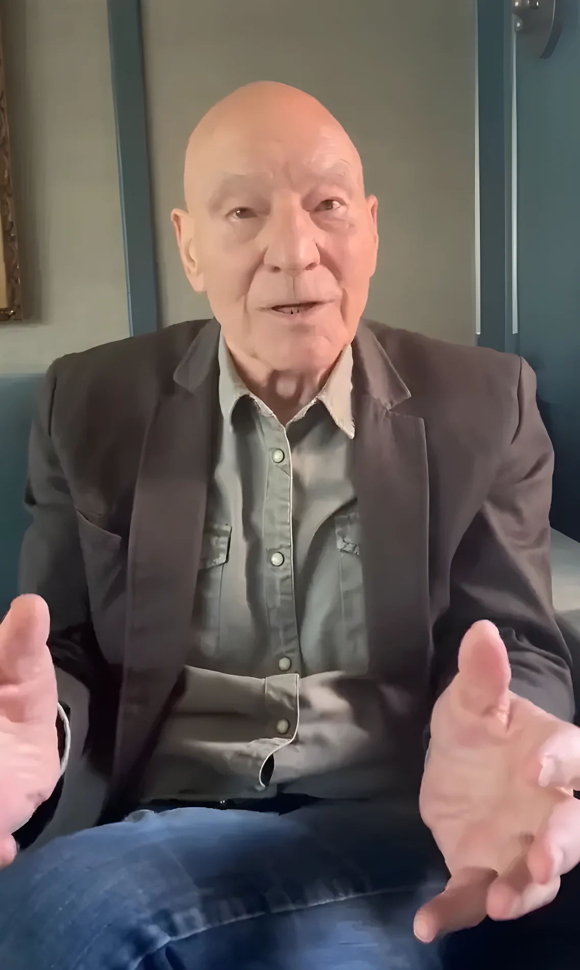Actor Patrick Stewart speaking while gesturing with his hands.