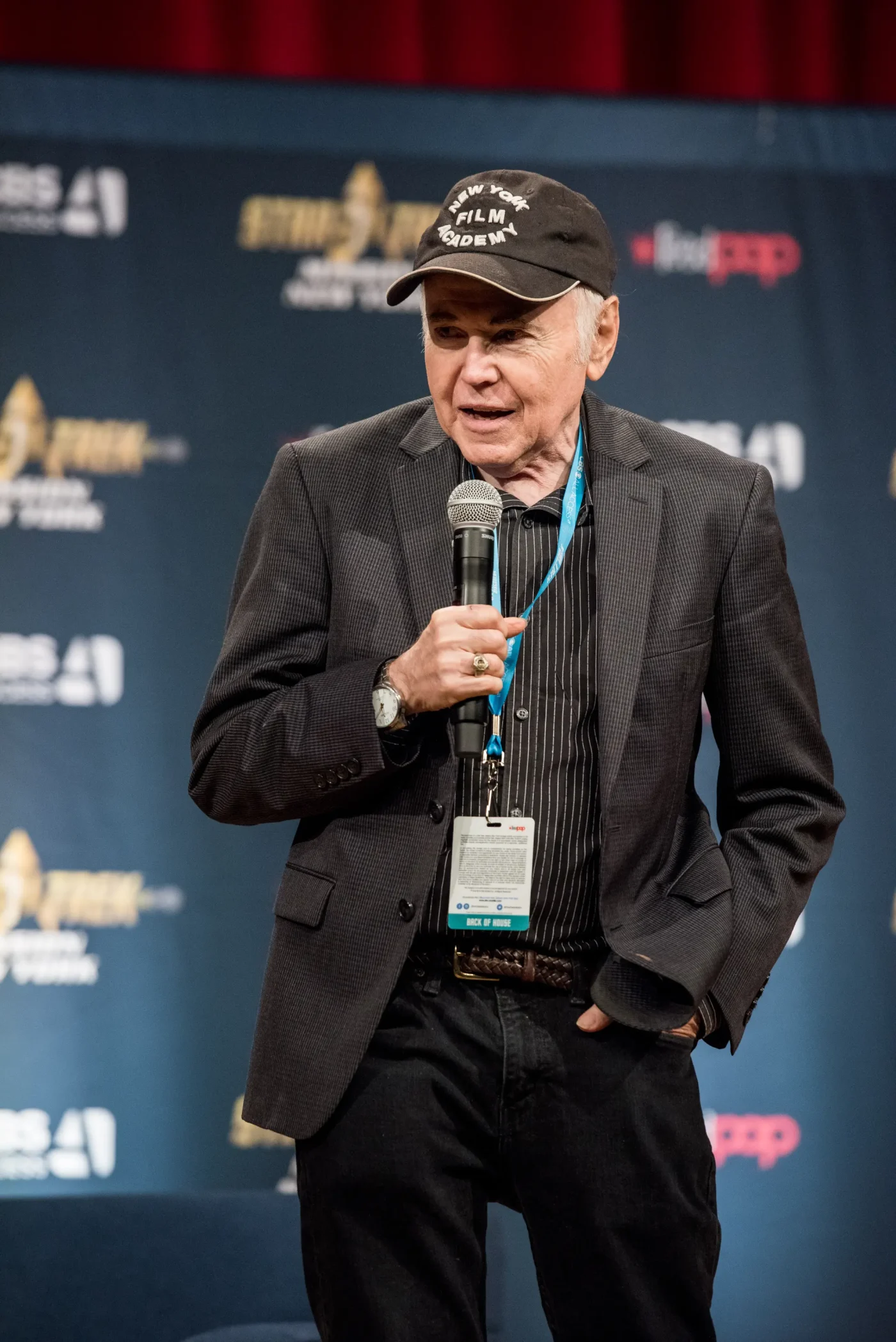 Actor Walter Koenig speaks into a microphone on stage at Star Trek: Mission New York.
