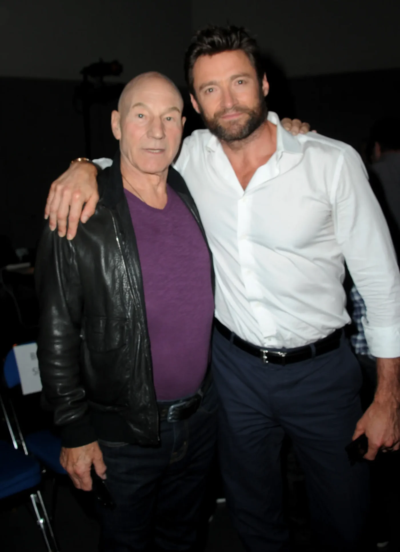 Actors Patrick Stewart and Hugh Jackman stand side-by-side with their arms around each other.