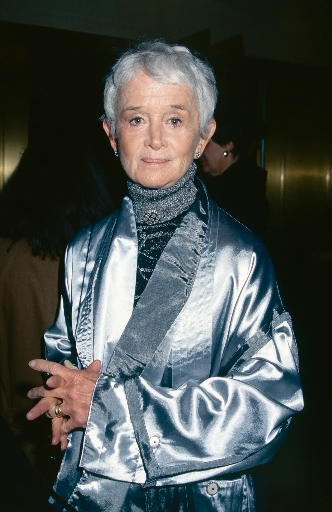 Actress Barbara Barrie wearing a silver jacket and a dark turtleneck with a decorative brooch.