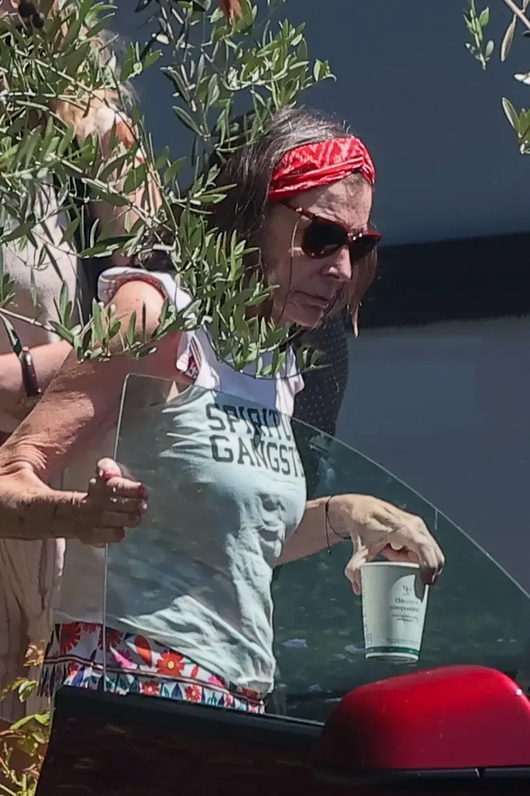 Actress Susan St James wearing a red headband and sunglasses, holding a coffee cup near a car.