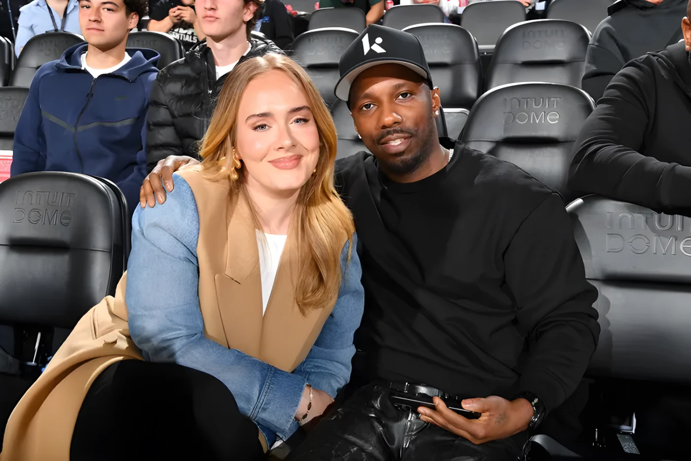 Adele and Rich Paul sitting together in an audience setting with others visible in the background