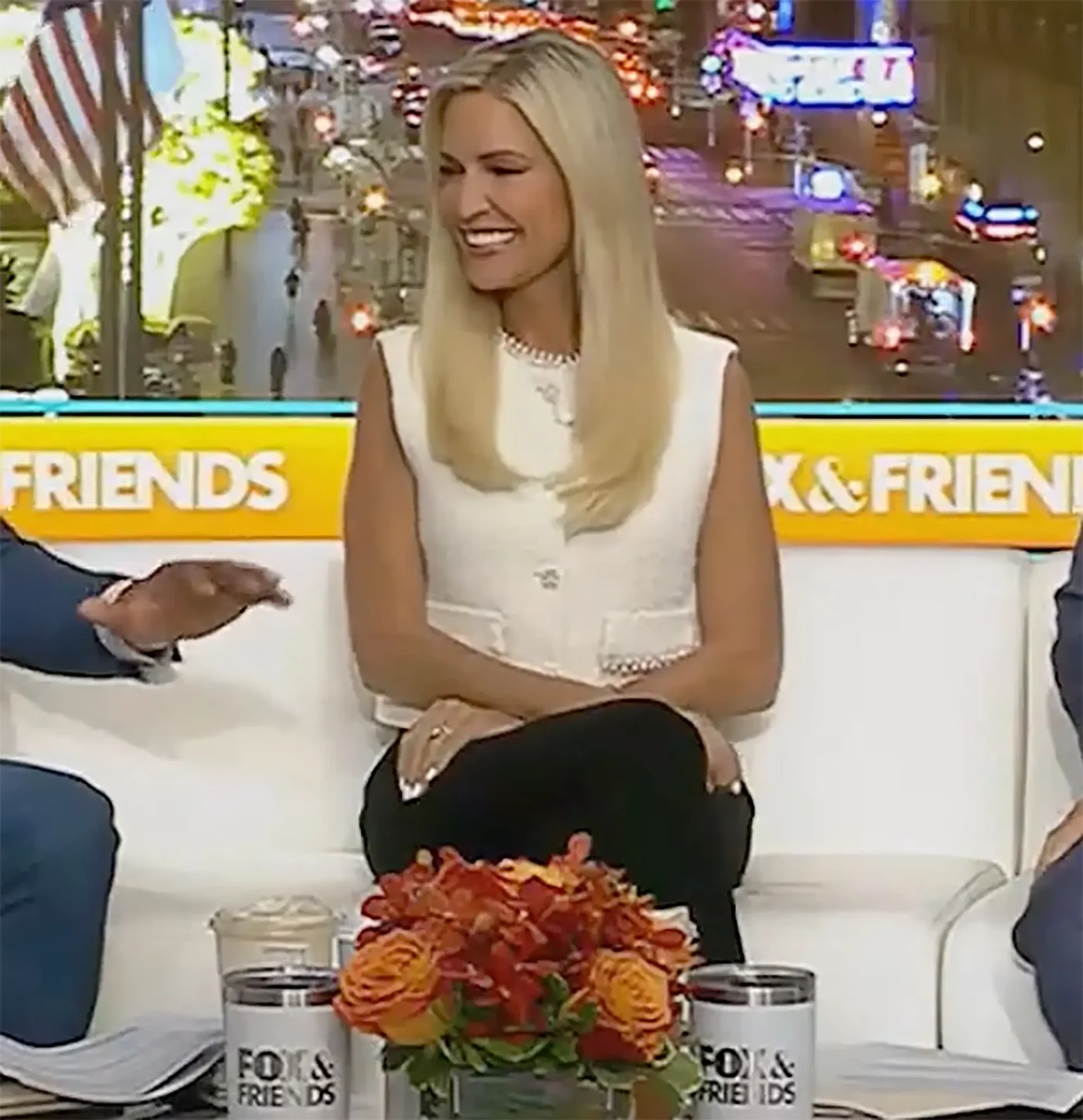 Ainsley Earhardt sitting on a white sofa on the set of Fox and Friends.