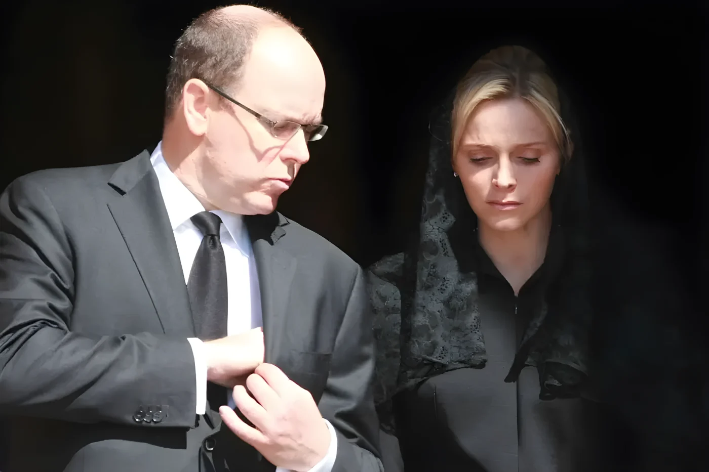 Albert II, Prince of Monaco, adjusts his suit next to Charlene, Princess of Monaco, in formal attire.