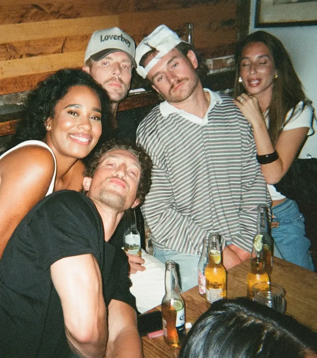 Amanda Batula and West Wilson pose with Kyle Cooke and friends while drinking beer in a dimly lit room.