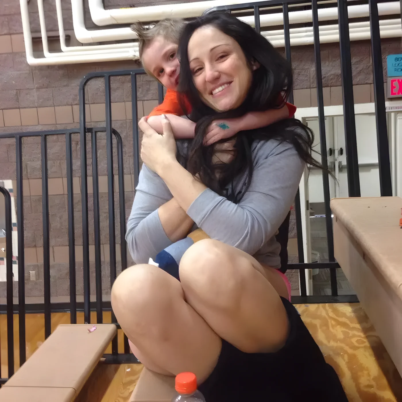 Amber Siyavus smiling while a young boy hugs her from behind, indoors.