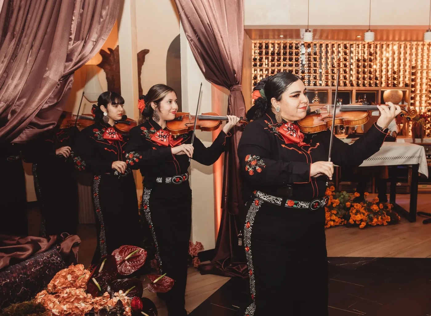 An all-female quartet wearing traditional black charro suits plays violins.