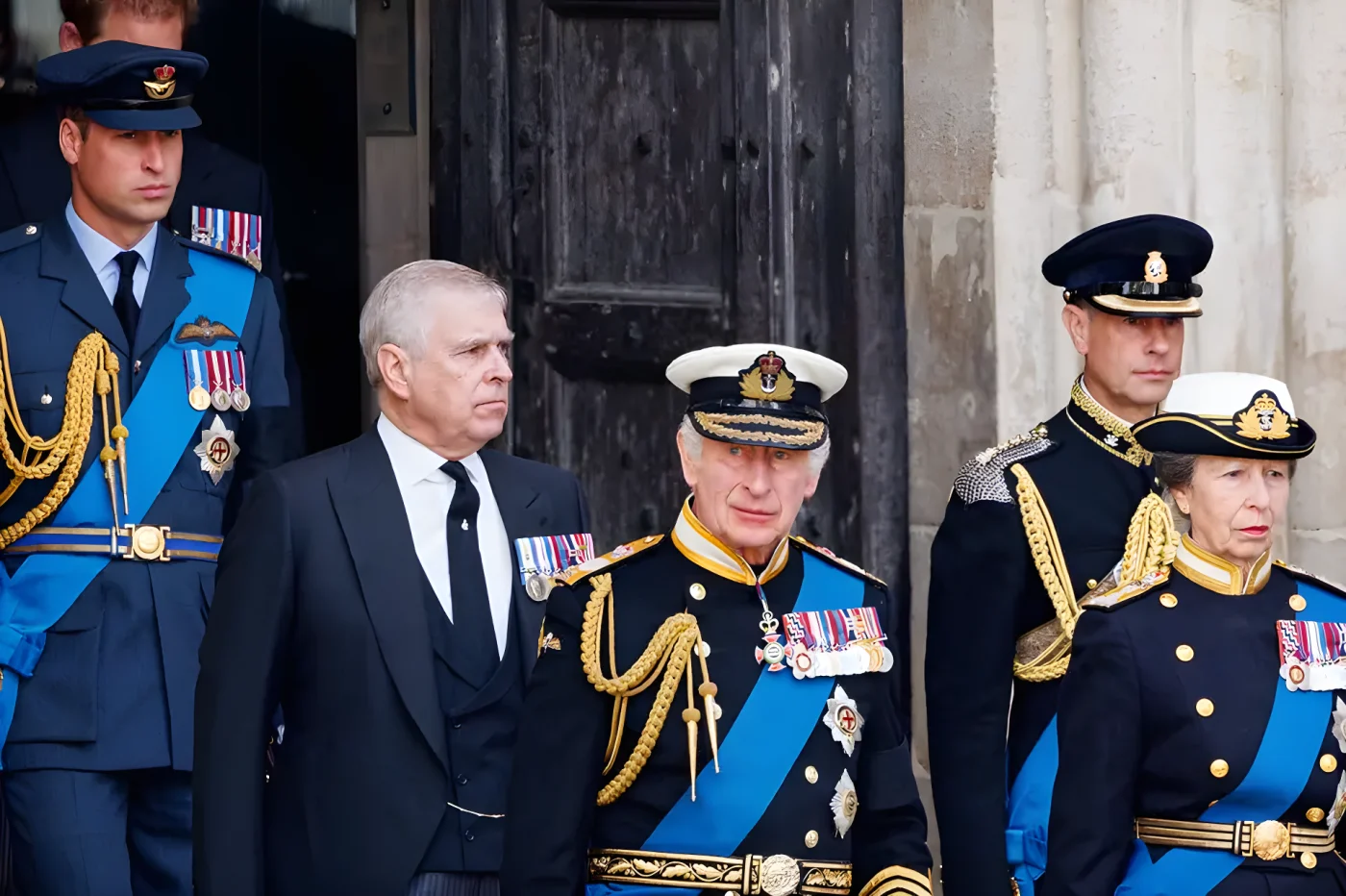 Andrew Mountbatten-Windsor in a blue suit behind King Charles