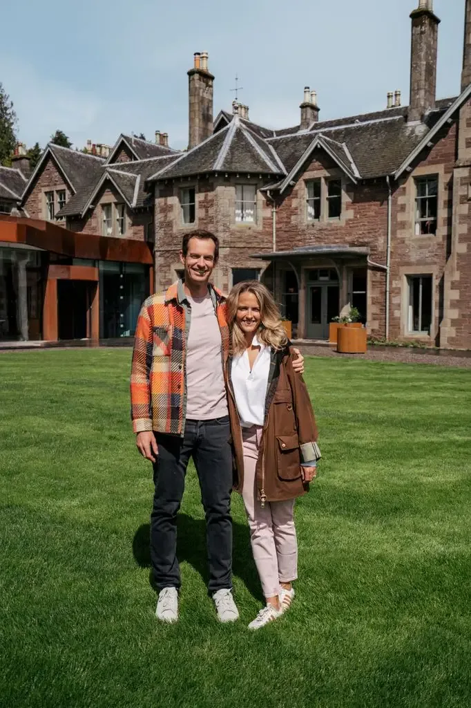 Andy Murray and wife Kim stand on a lawn in front of a large house, smiling.