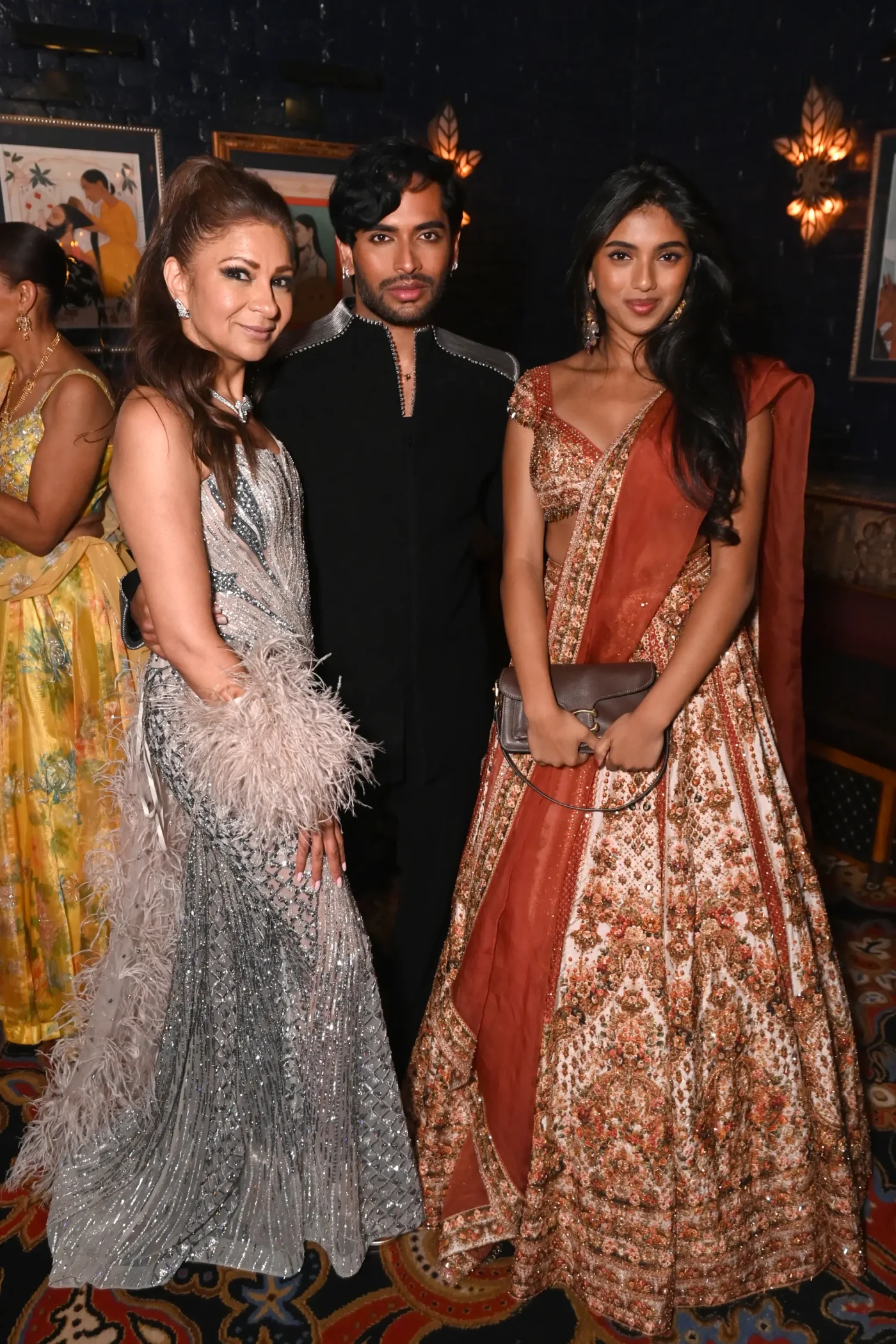 Anjula Acharia, Aditya Madiraju, and Avantika Vandanapu posing together indoors, dressed in formal event attire.