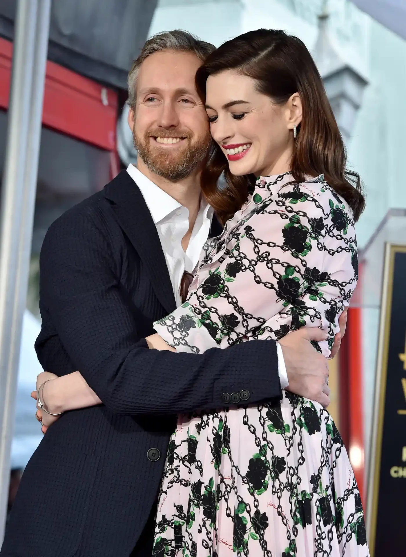 Anne Hathaway embracing another individual both smiling warmly