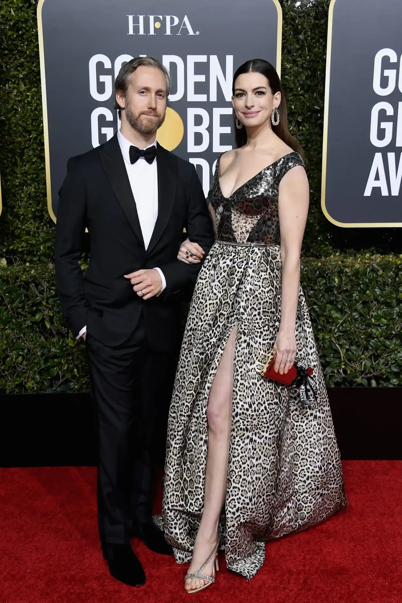 Anne Hathaway posing on the red carpet with a companion wearing an evening gown