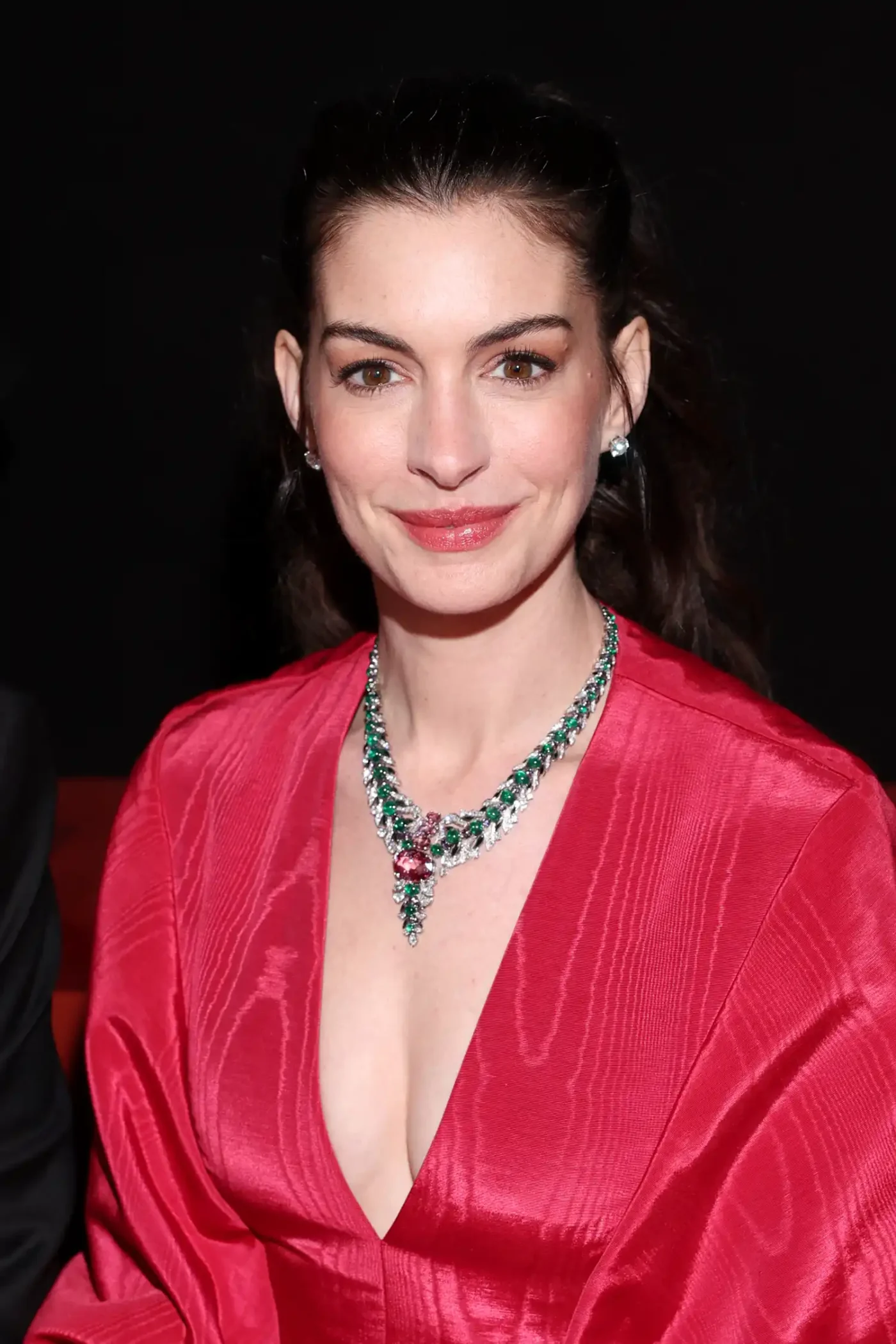 Anne Hathaway smiling at an event wearing a dress and a necklace