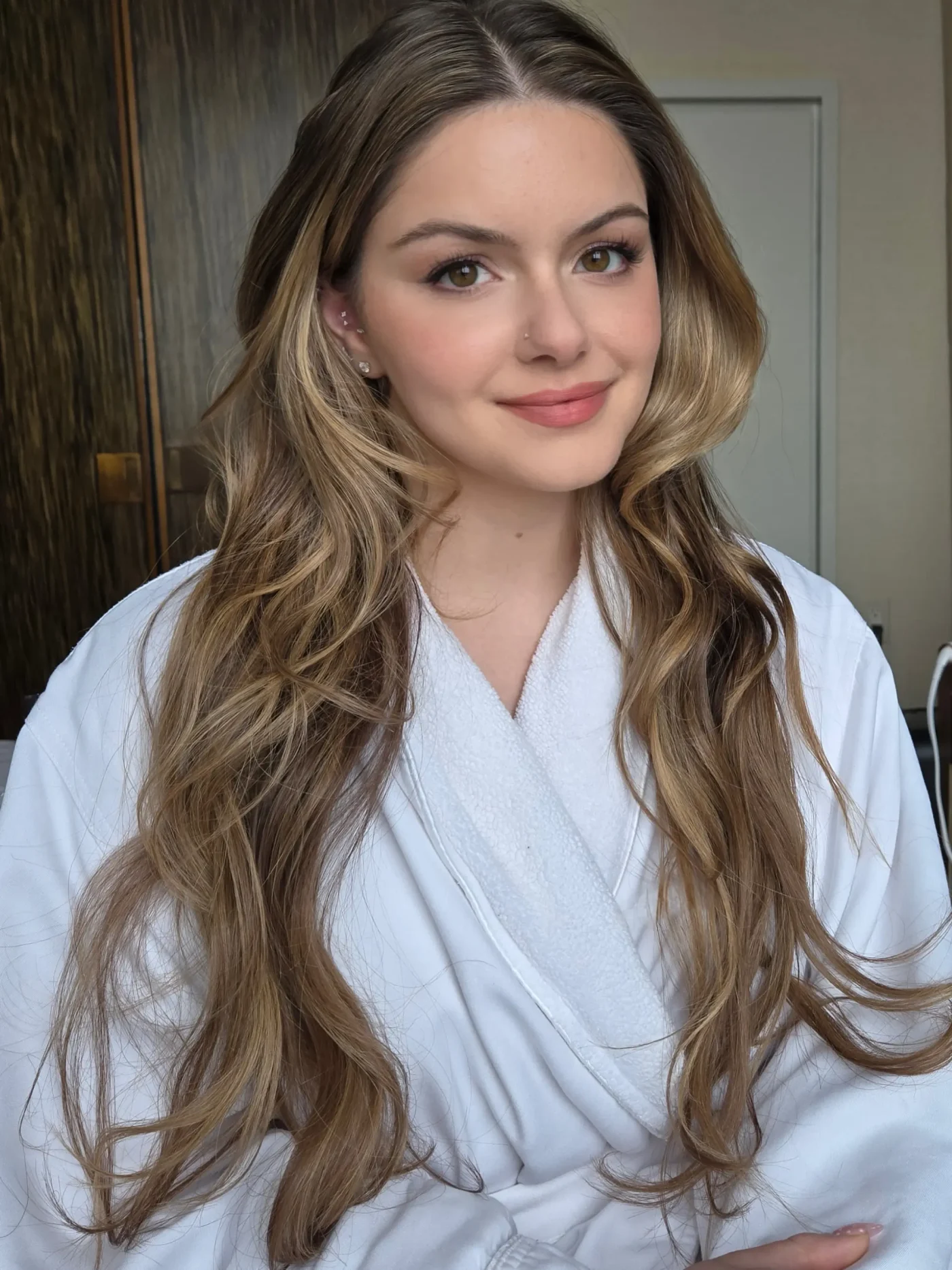 Ariel Winter wearing a white bathrobe with her long brown hair styled in soft waves.
