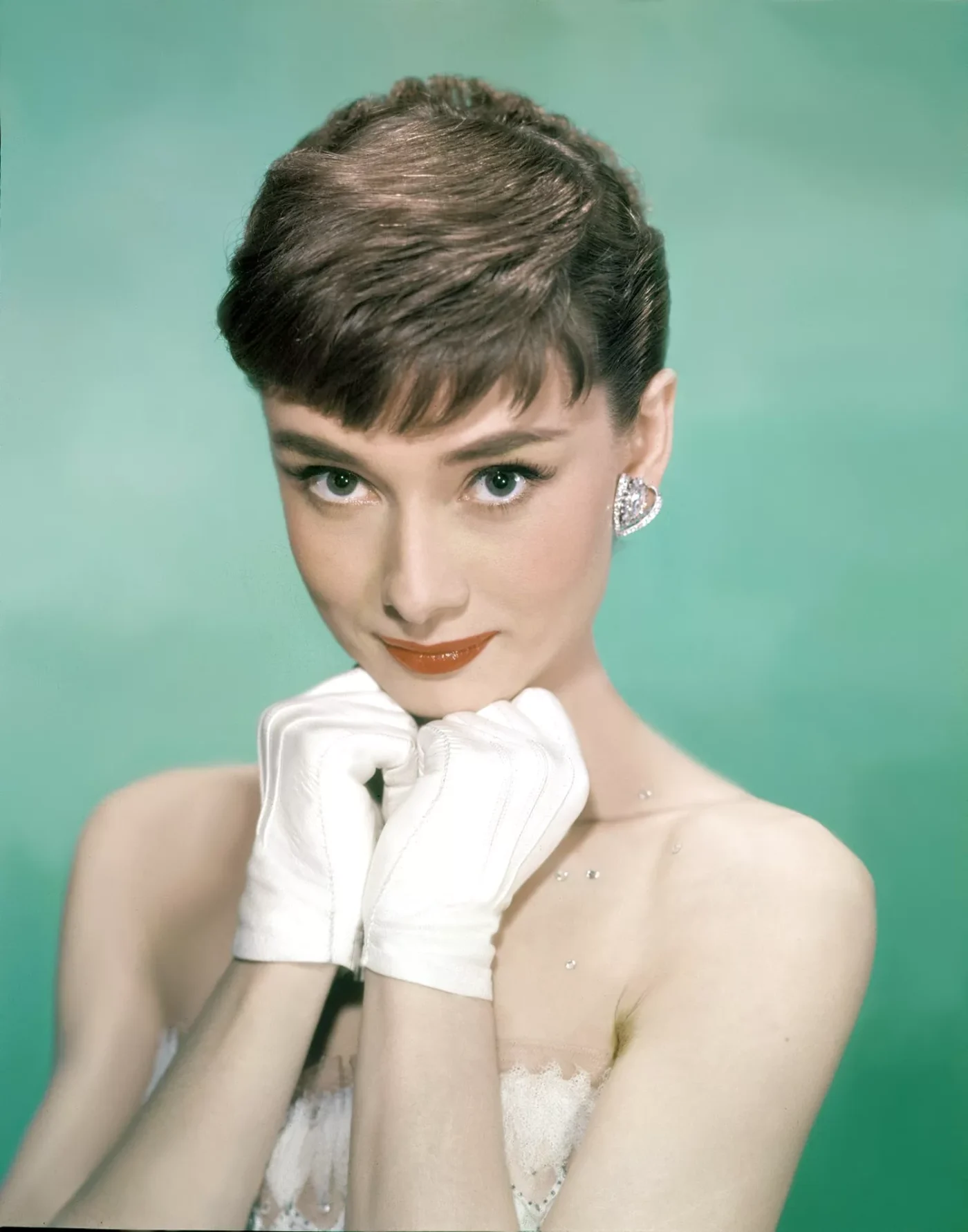 Audrey Hepburn against a green background with pixie hairstyle while wearing white gloves