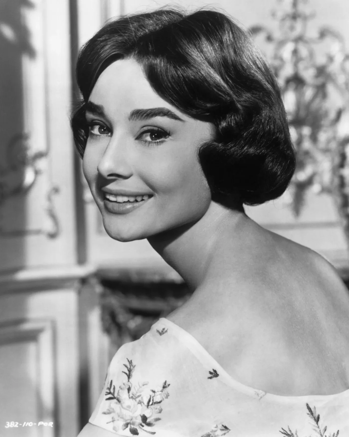 Audrey Hepburn in a posed photograph facing partially backward and smiling